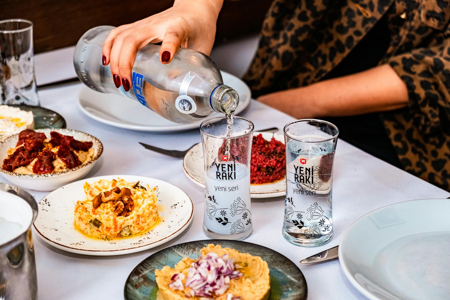 예니 라키(Yeni Rakı) 술잔에 물을 붓는 모습과 다양한 터키식 메제(Meze) 요리가 차려진 이스탄불의 술자리 풍경