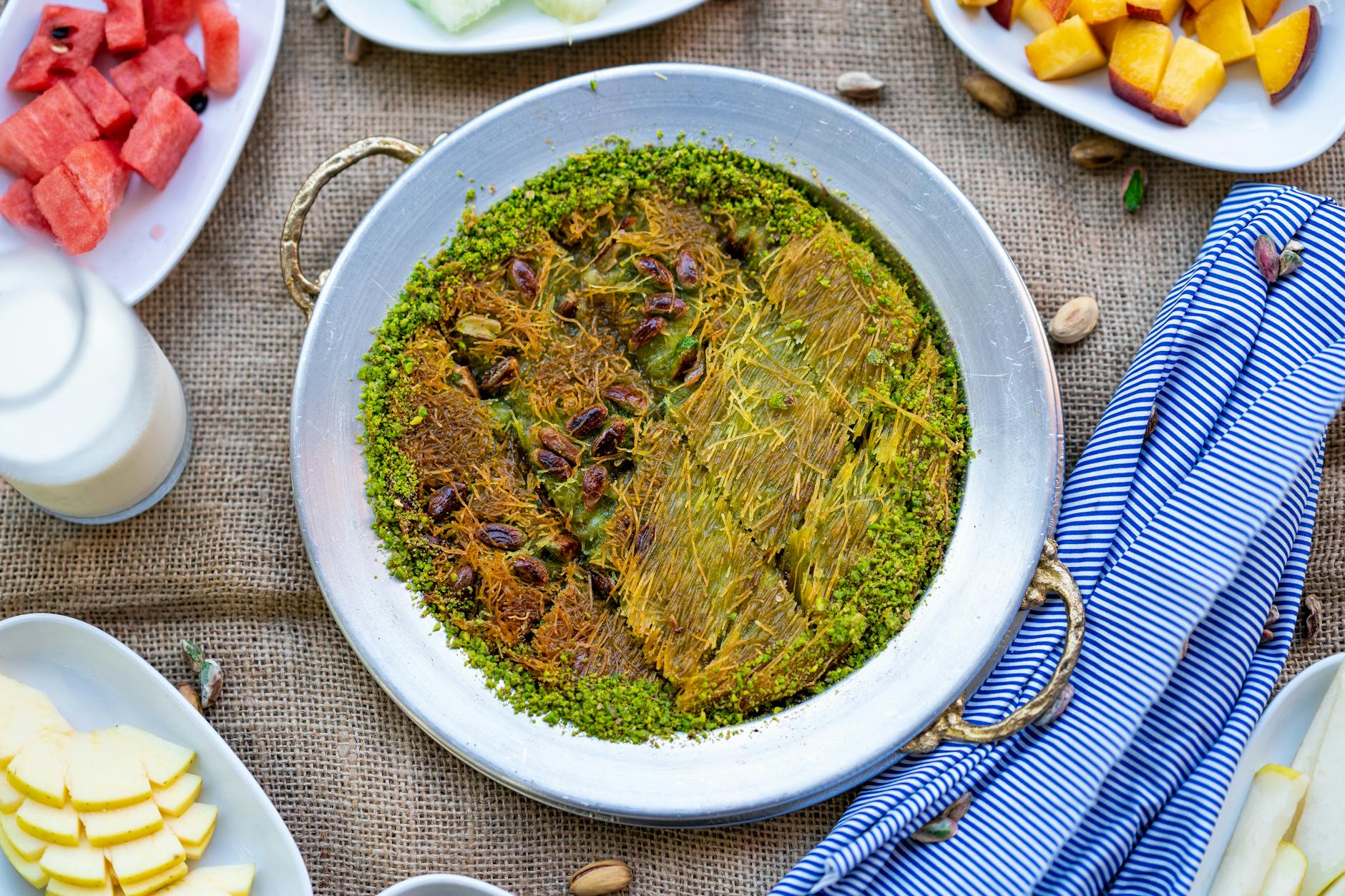 은색 쟁반에 담겨 피스타치오 가루로 장식된 노릇하고 달콤한 터키 정통 퀴네페의 전체 모습이다.