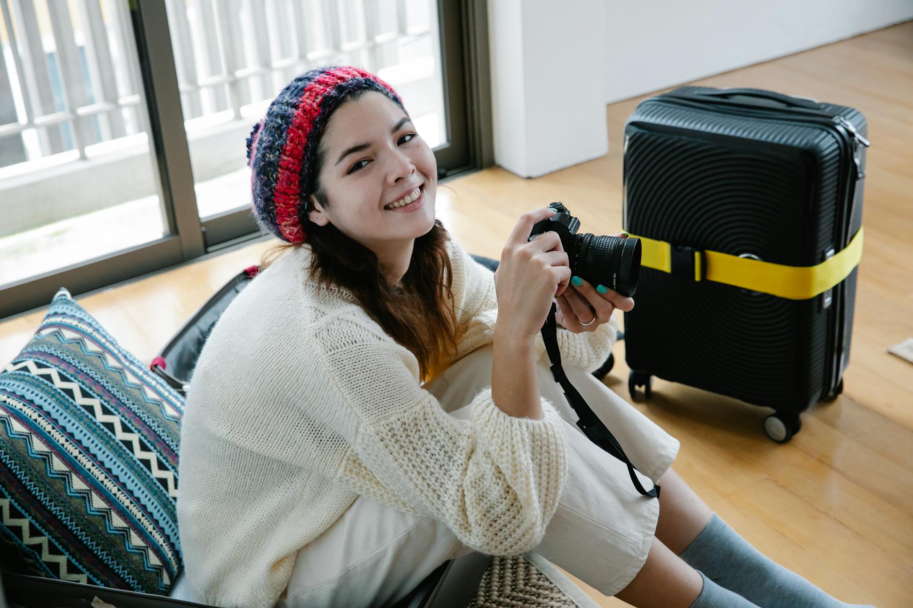 비니와 스웨터를 착용하고 여행을 준비하는 여성이 미소 짓습니다.